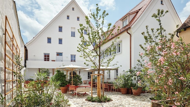 A courtyard with a white building, outdoor seating, and potted plants. - Engelwirt Hotel & Apartments (Berching)