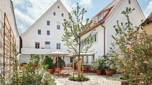 A courtyard with a white building, outdoor seating, and potted plants. - Engelwirt Hotel & Apartments (Berching)