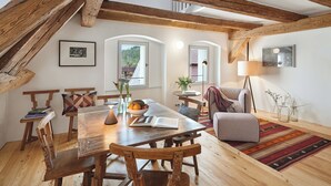 A cozy loft-style room with exposed wooden beams, a dining area with a wooden table and chairs, and a comfortable seating area with a sofa and armchair. - Engelwirt Hotel & Apartments (Berching)