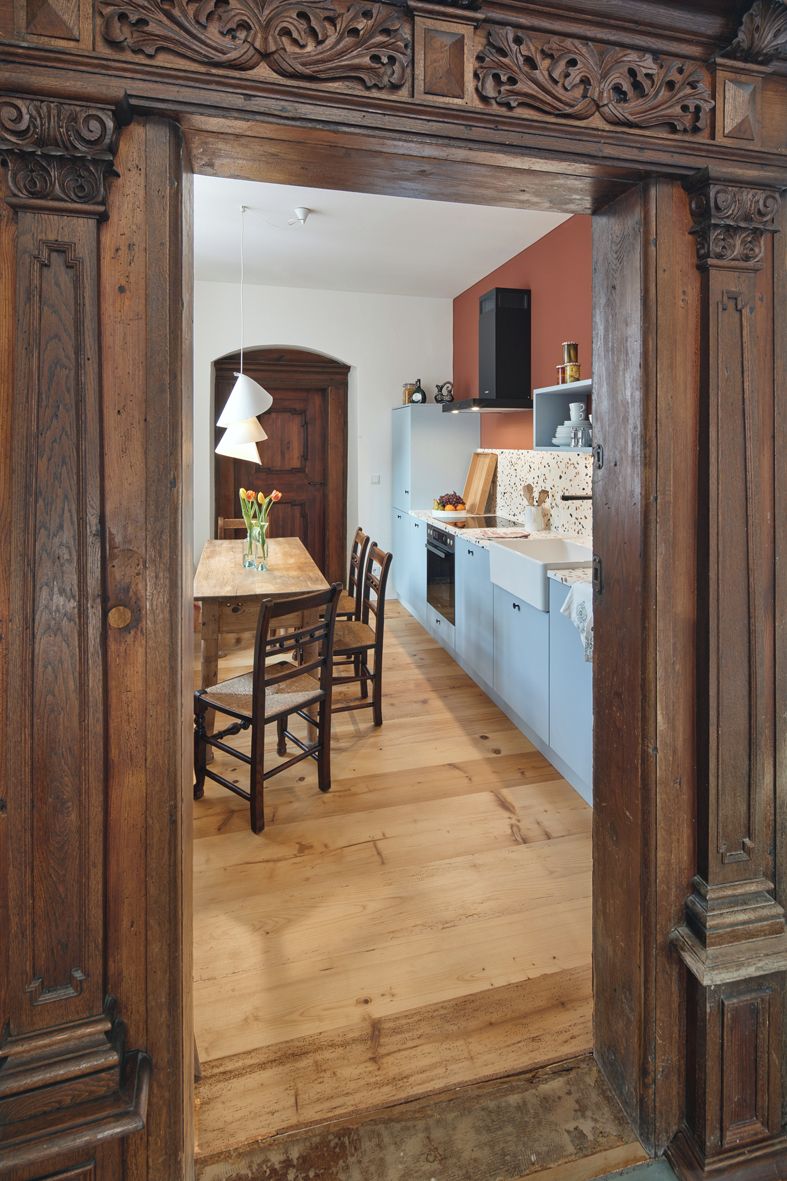 A wooden dining area with a table and chairs, a hanging light fixture, and a kitchen with blue cabinets and a white countertop.