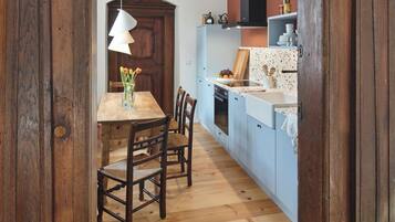 A wooden dining area with a table and chairs, a hanging light fixture, and a kitchen with blue cabinets and a white countertop.