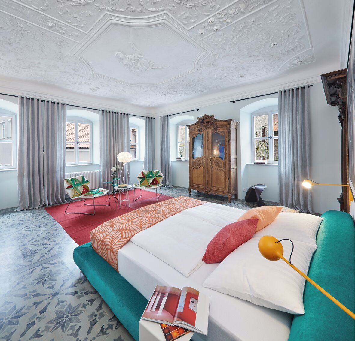 A spacious bedroom with a large bed, a wooden wardrobe, and a red carpet.