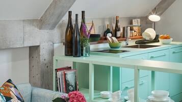 A kitchen with teal cabinetry, a countertop with wine bottles, a sink, and a dining area with white plates and bowls.