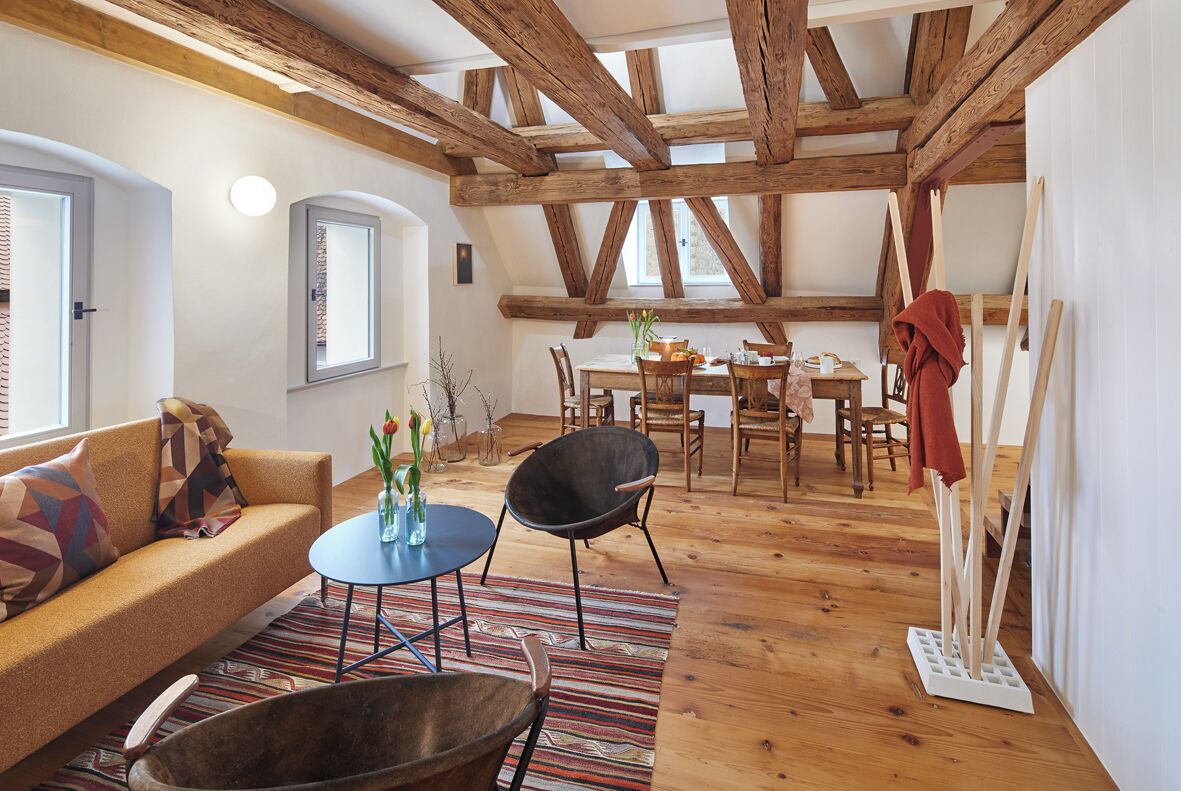 Una sala de estar acogedora con techo de madera, un sofá, una mesa redonda de centro y una zona de comedor con sillas y una mesa.