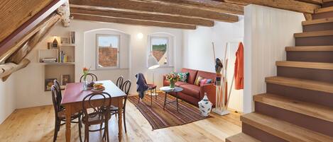 Un loft espacioso con vigas de madera a la vista, comedor, sofá y escalera.