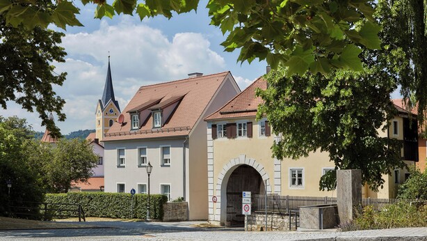 A historic building with a prominent tower, a large arched entrance, and a paved street in front. - Engelwirt Hotel & Apartments (Berching)