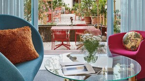 A modern living room with a glass coffee table, a blue armchair, and a red armchair with a floral cushion. - Engelwirt Hotel & Apartments (Berching)