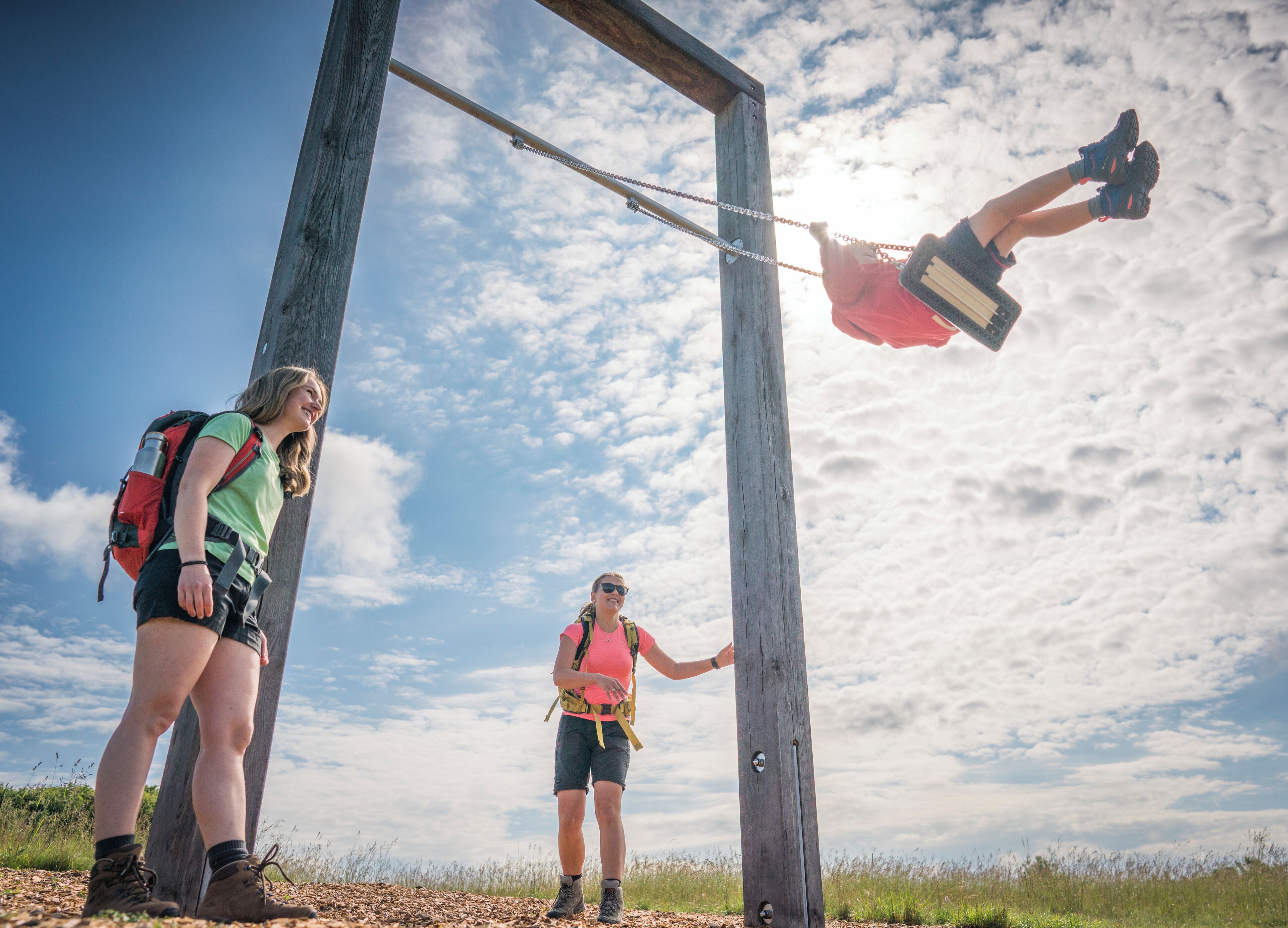Two people climbing a wooden structure with a metal chain, set against a clear sky.