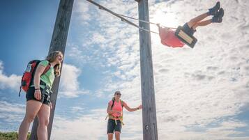 Two people climbing a wooden structure with a metal chain, set against a clear sky.