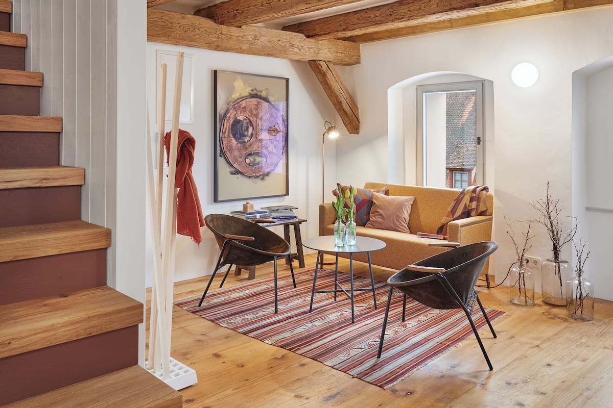 A modern living room with a staircase, wooden beams, a sofa, a coffee table, and a painting.