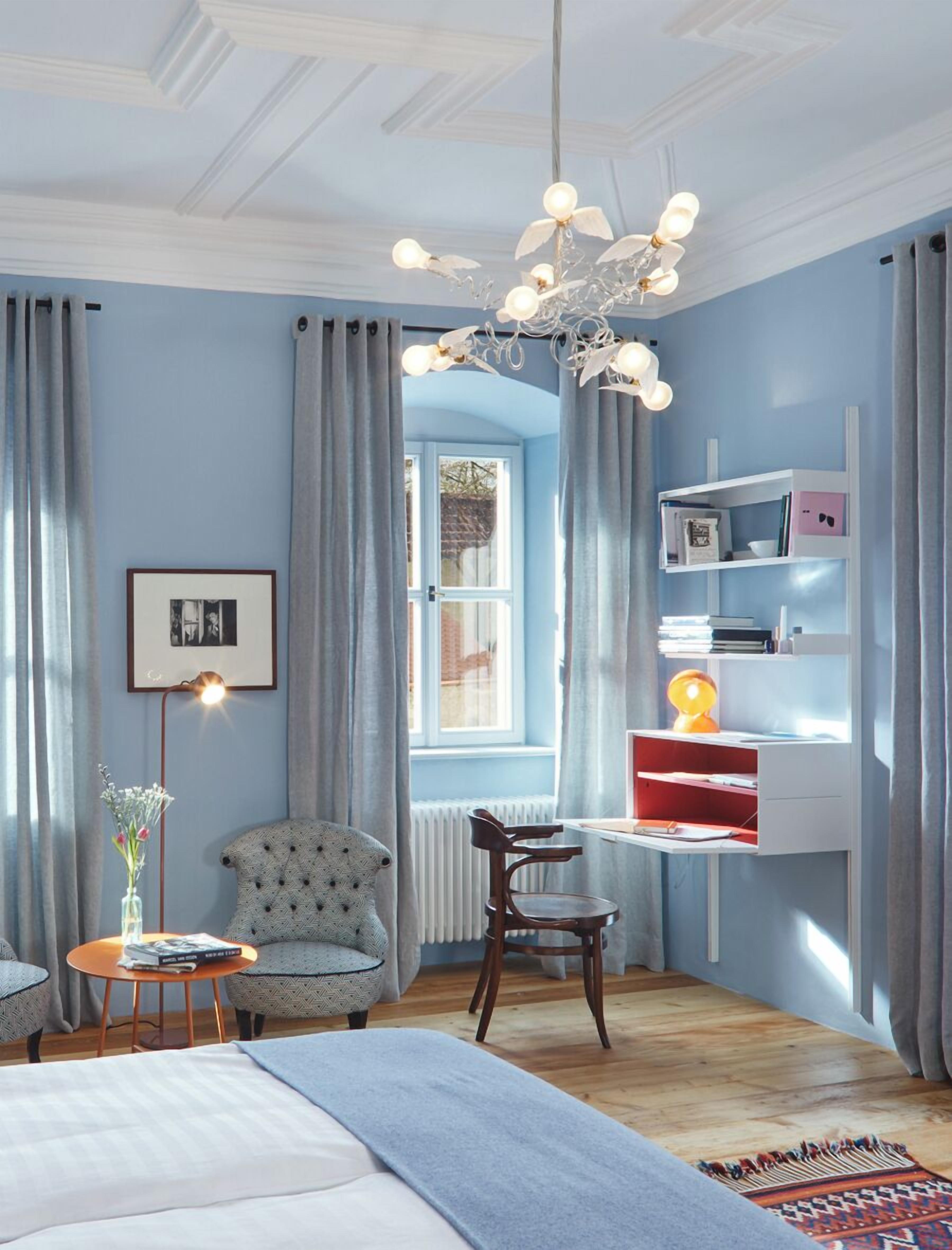A bedroom with a bed, a desk, a chair, a bookshelf, a radiator, and a window with curtains.
