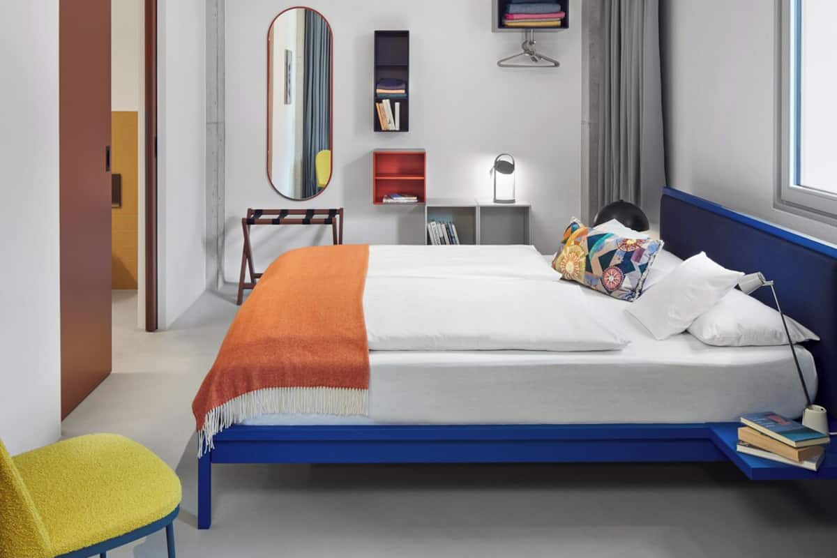 A modern hotel room with a large bed, a desk, a chair, and a mirror.