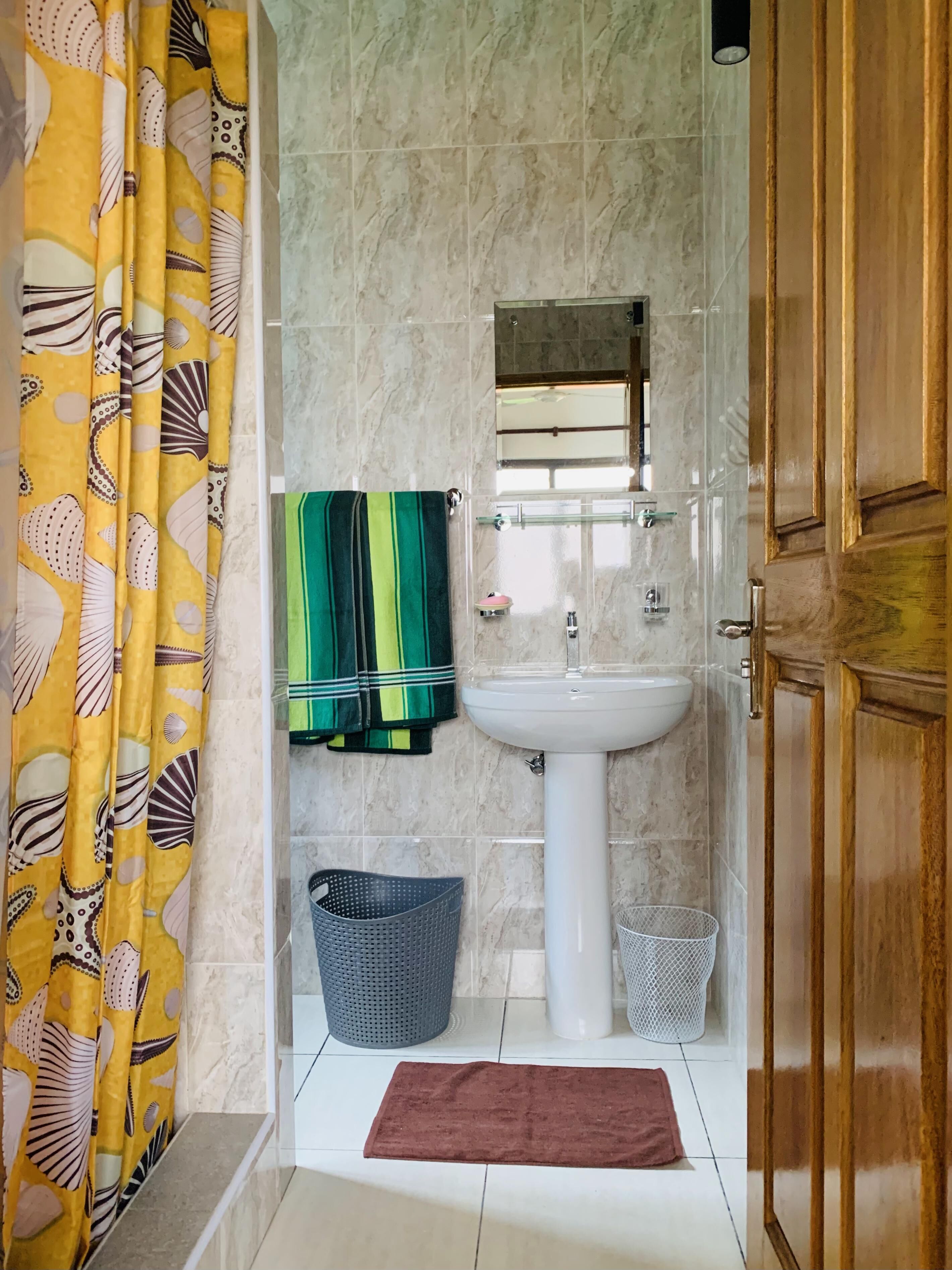 Un baño con lavamanos, espejo, toallero, cortina de ducha y puerta de madera.