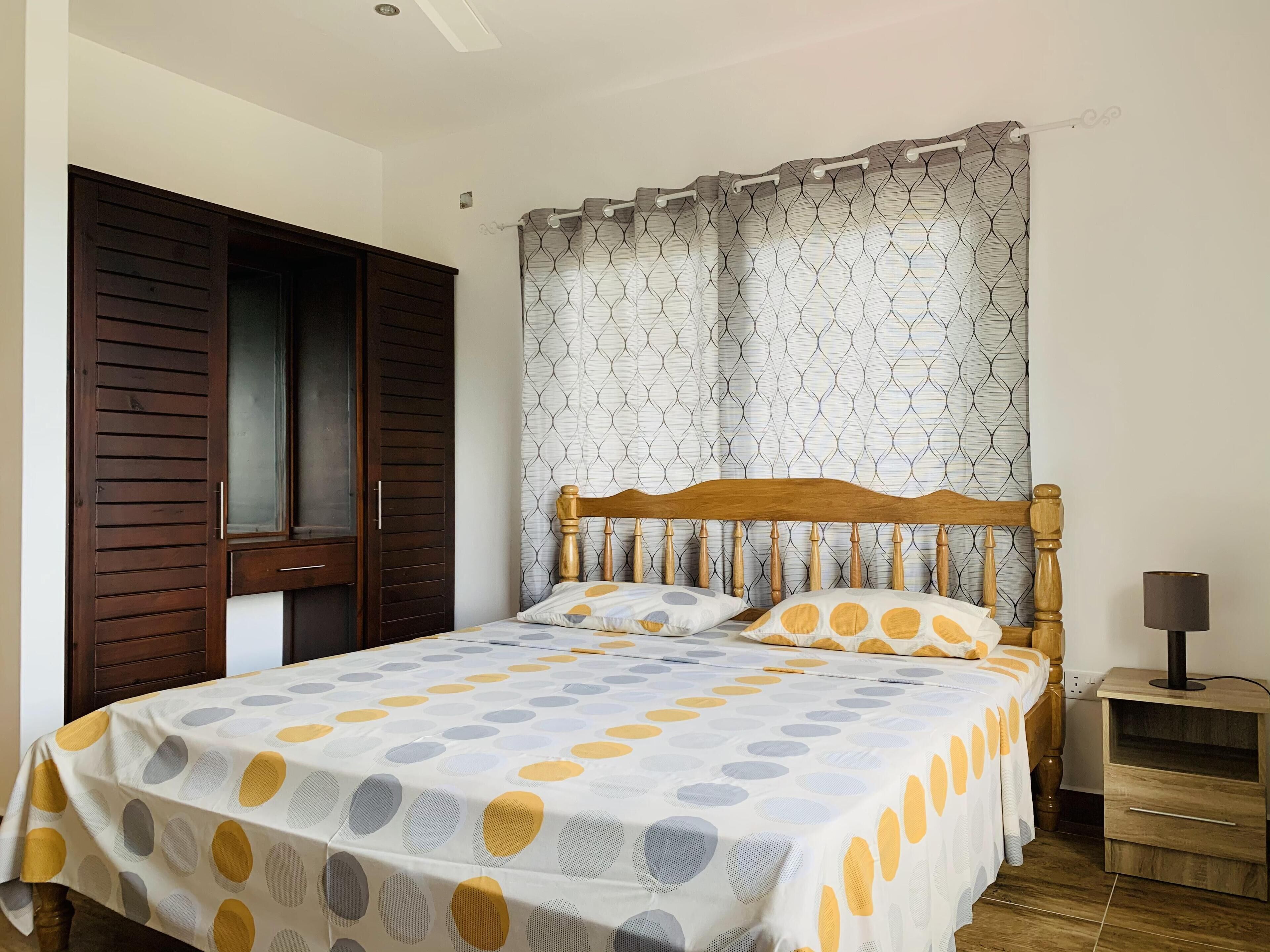 A bedroom with a bed, wooden headboard, curtains, a nightstand, and a lamp.