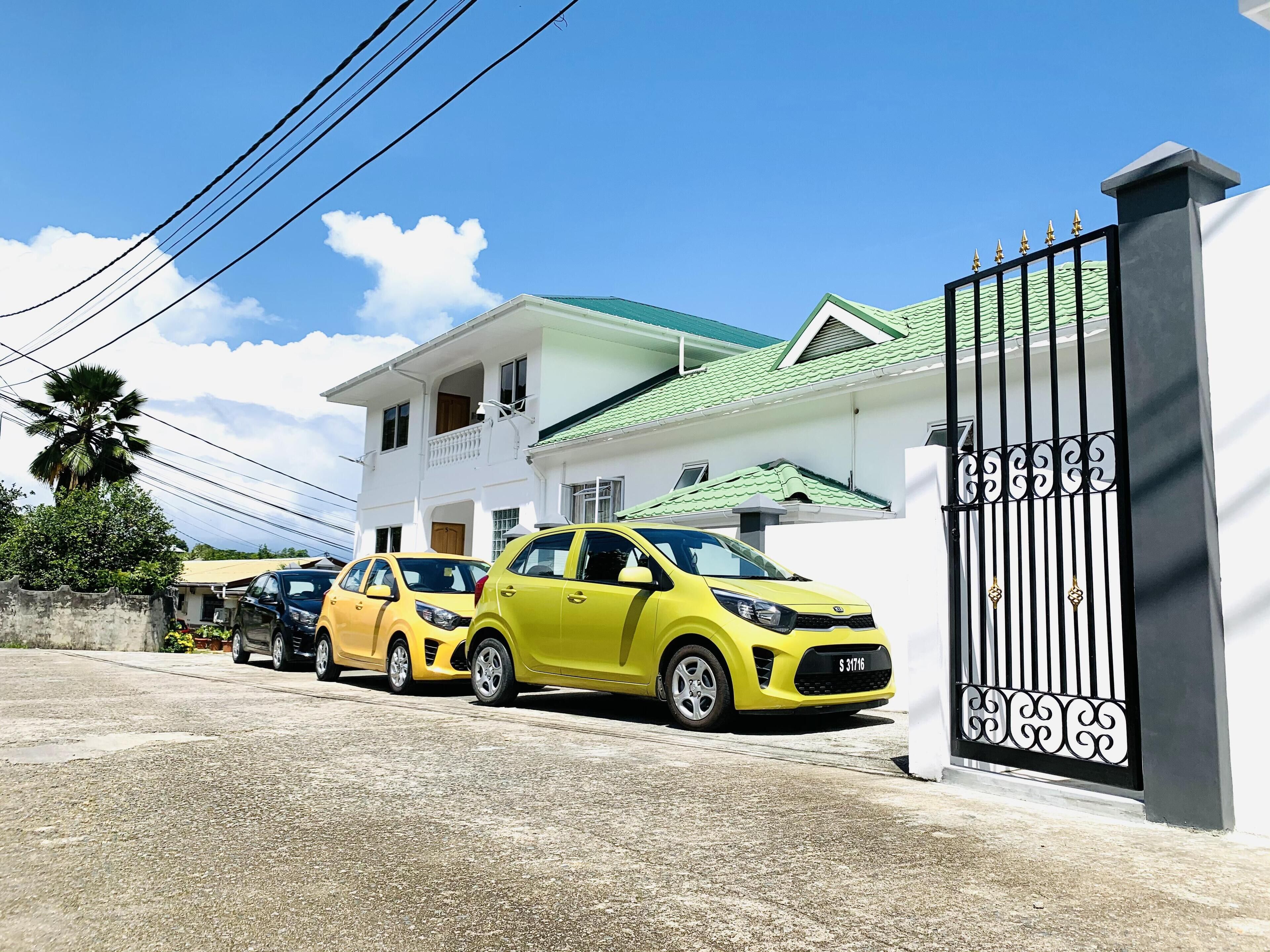 A gated residential area with a white house featuring a green roof and a black gate.