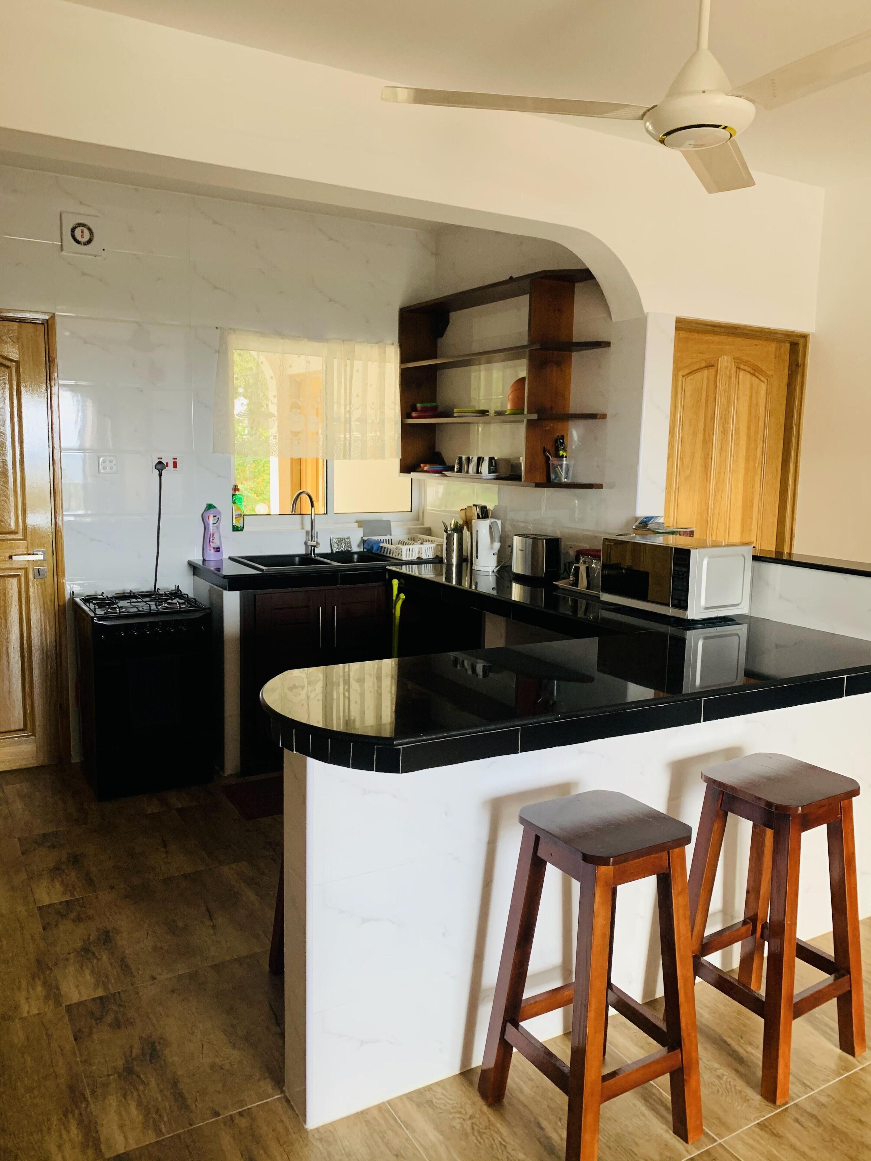 A modern kitchen with a central island, wooden stools, and built-in shelves.