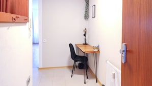 Un couloir étroit avec une porte en bois, un radiateur, une petite table avec une chaise et une plante accrochée au mur.