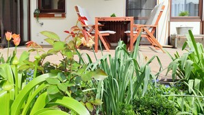 Une terrasse avec une table et des chaises en bois, entourée d’une végétation luxuriante et de fleurs.