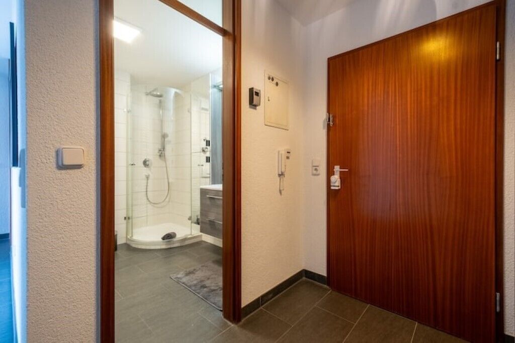 Hotellihuoneessa on puinen ovi, suihkutila ja pieni ohjauspaneeli seinässä.
