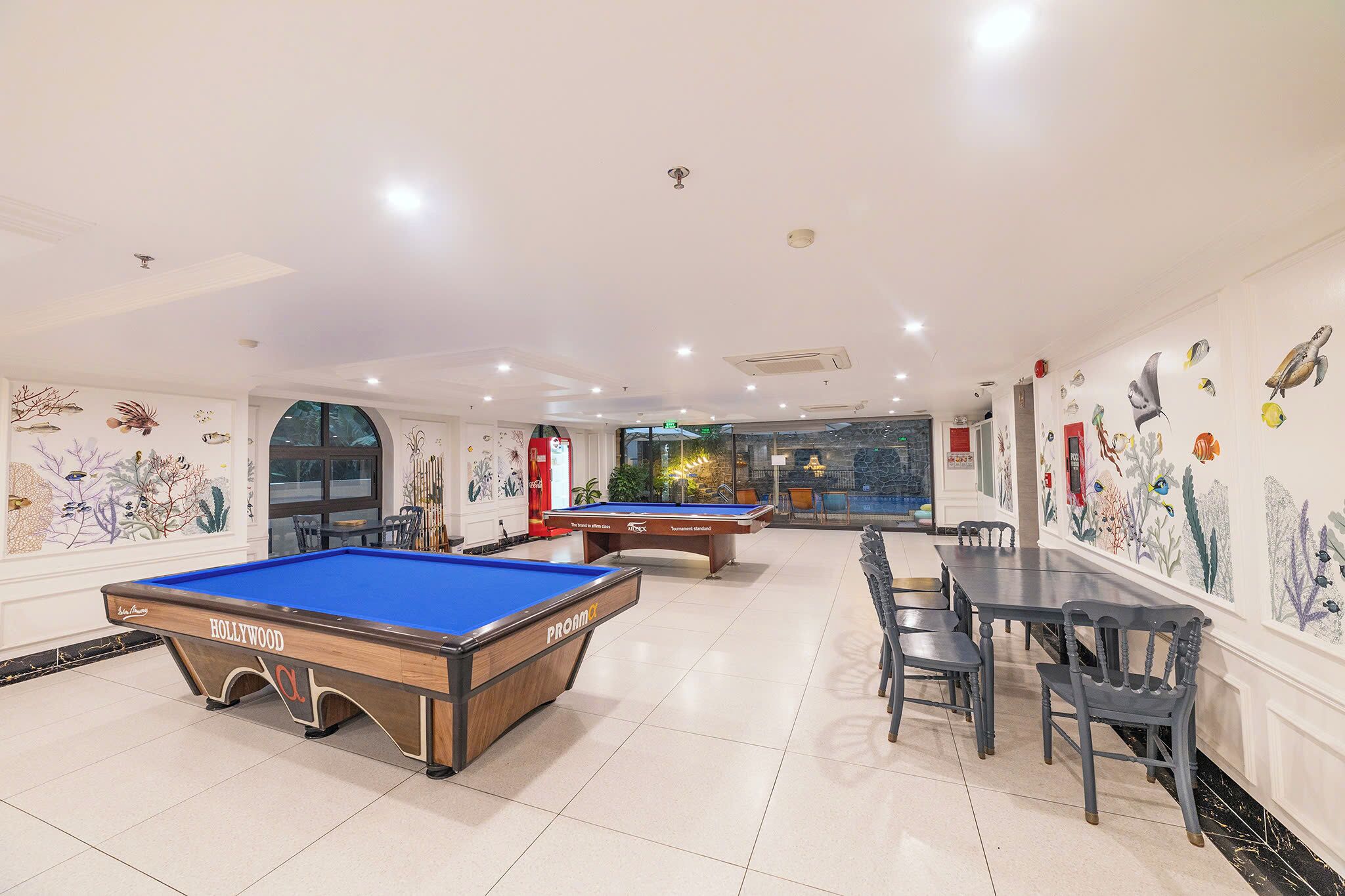A pool table with a blue felt top and a wooden frame, a billiards table, and a dining area with chairs and tables.