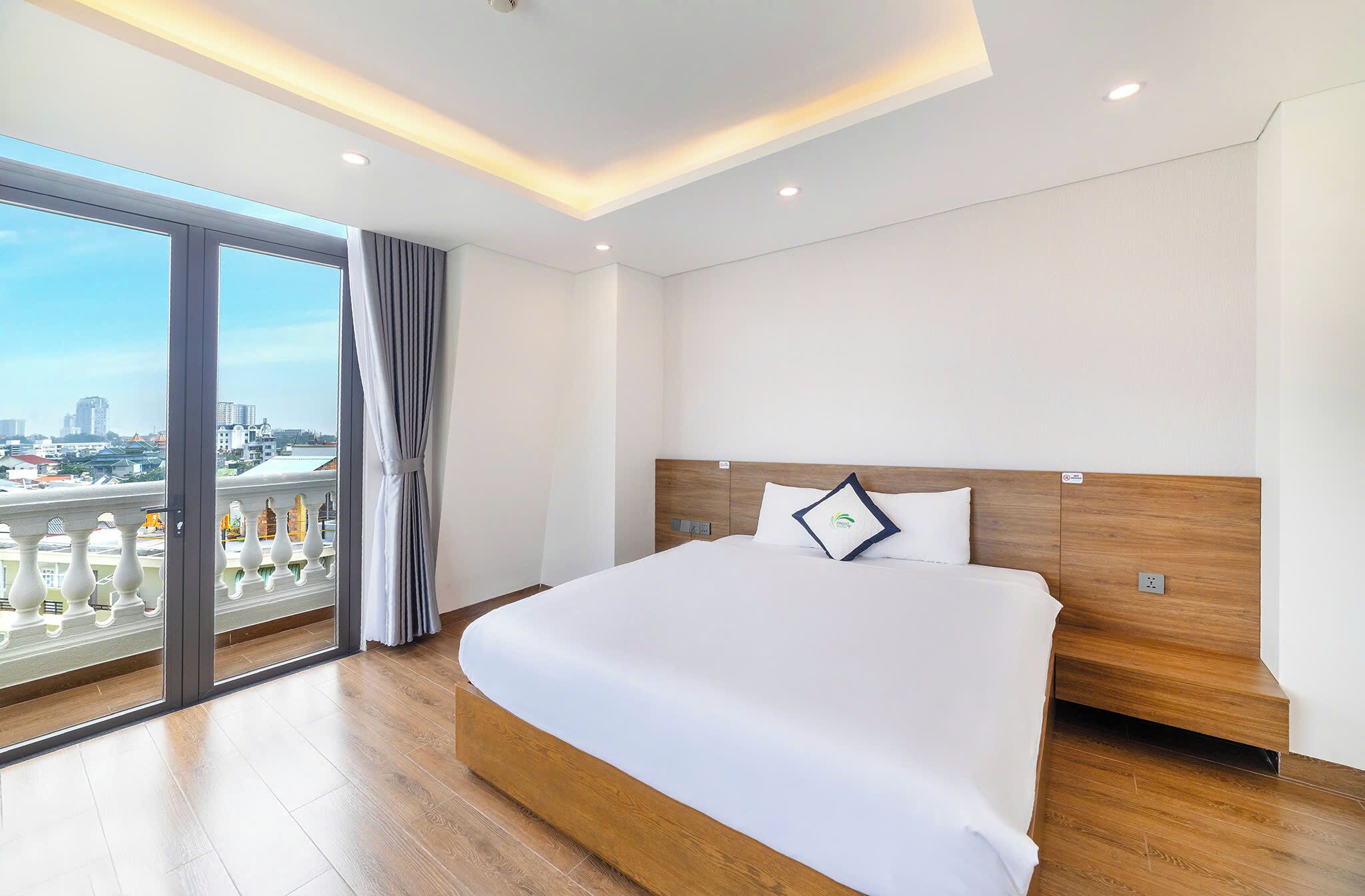 A modern hotel room with a large bed, wooden headboard, and a balcony with a city view.