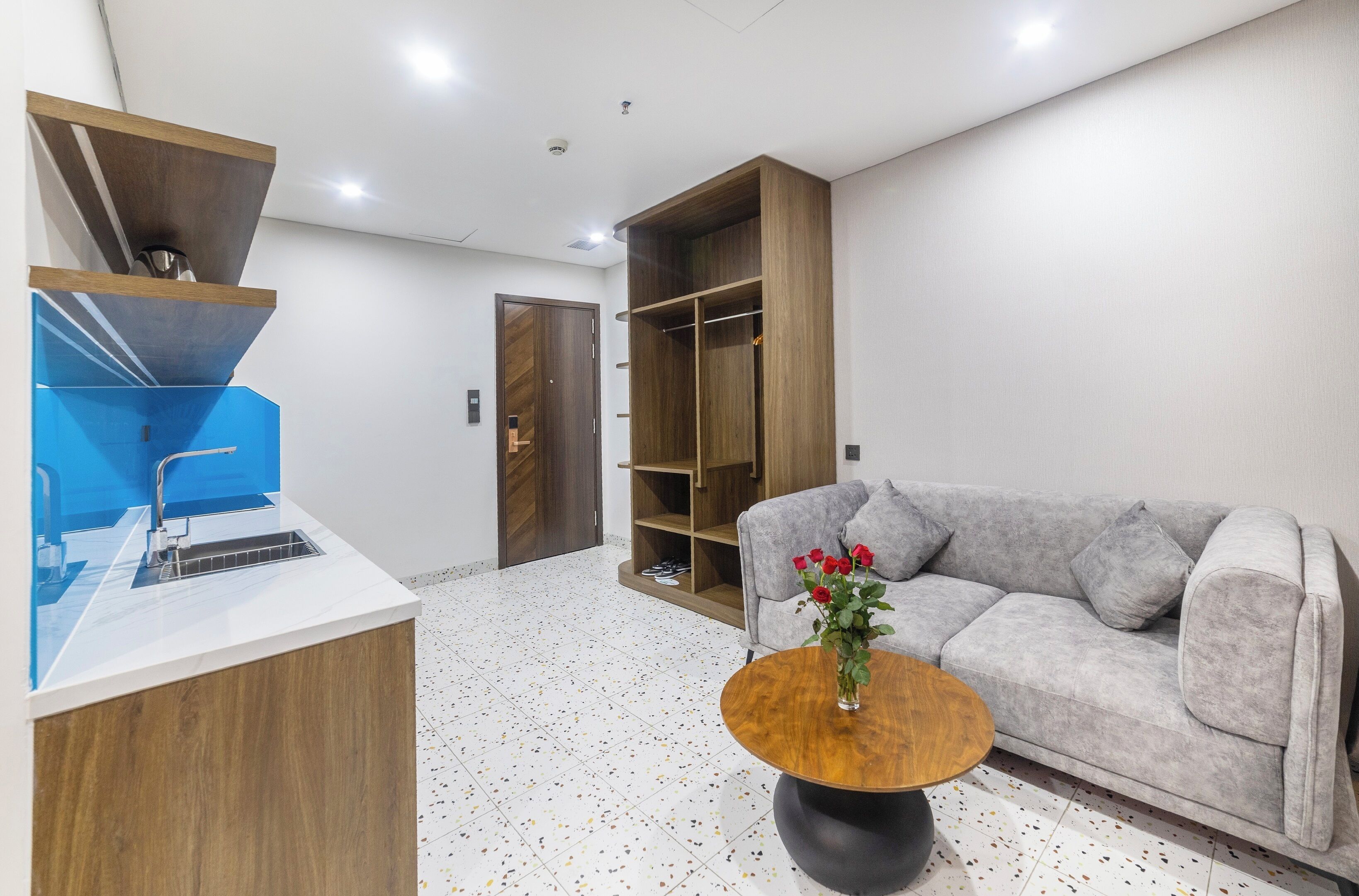 Uma sala de estar moderna com um sofá cinza, uma mesa de centro com um vaso de rosas vermelhas e um armário de madeira com um objeto azul em cima.