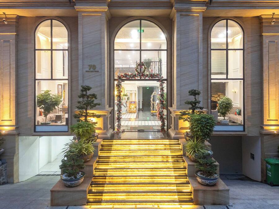 Une entrée imposante, avec un escalier menant à un hall, de part et d’autre duquel se trouvent de grandes fenêtres et des plantes en pot.