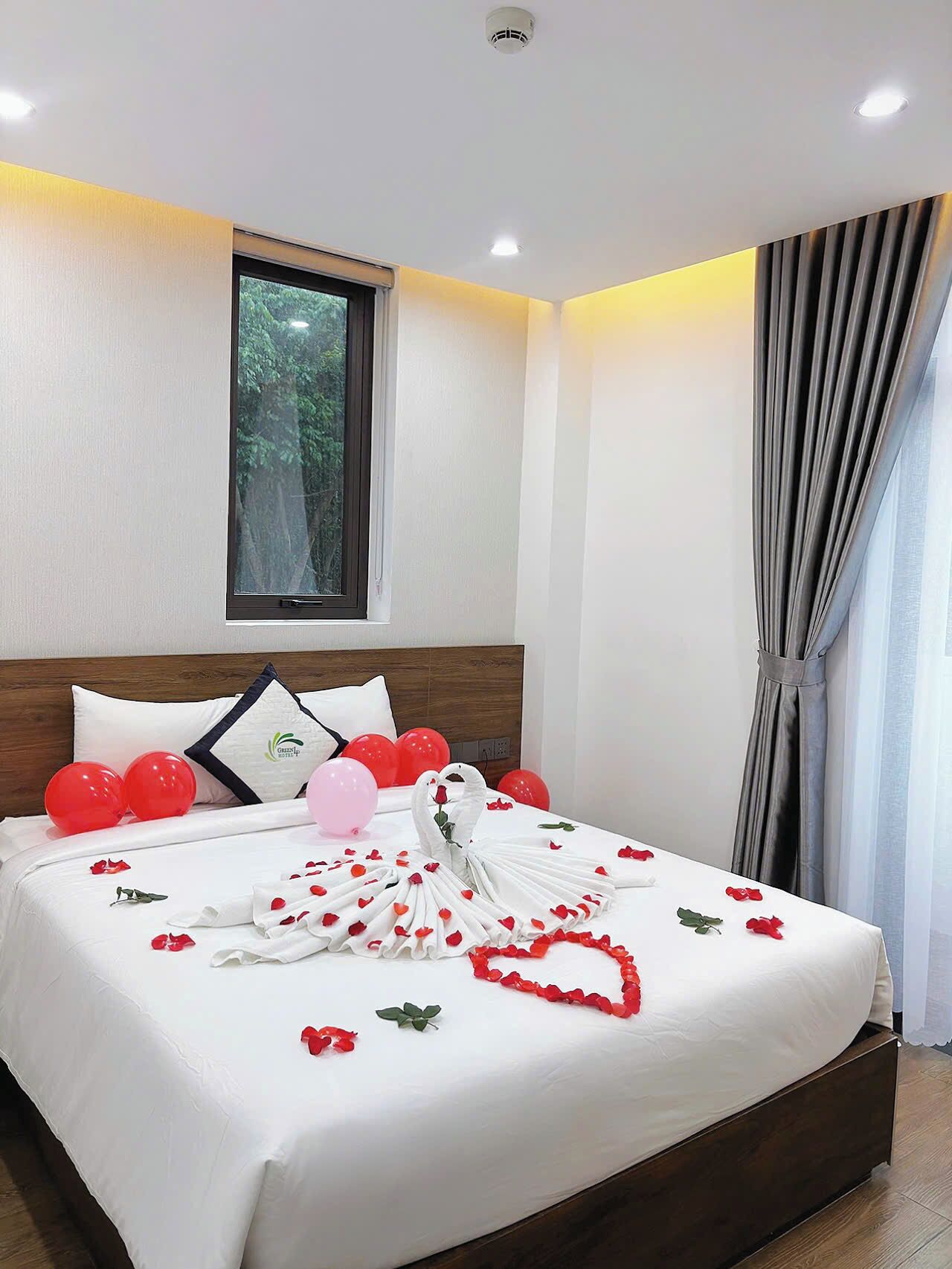 A hotel room with a neatly made bed, a window with a view of trees, and a curtain on the right side.