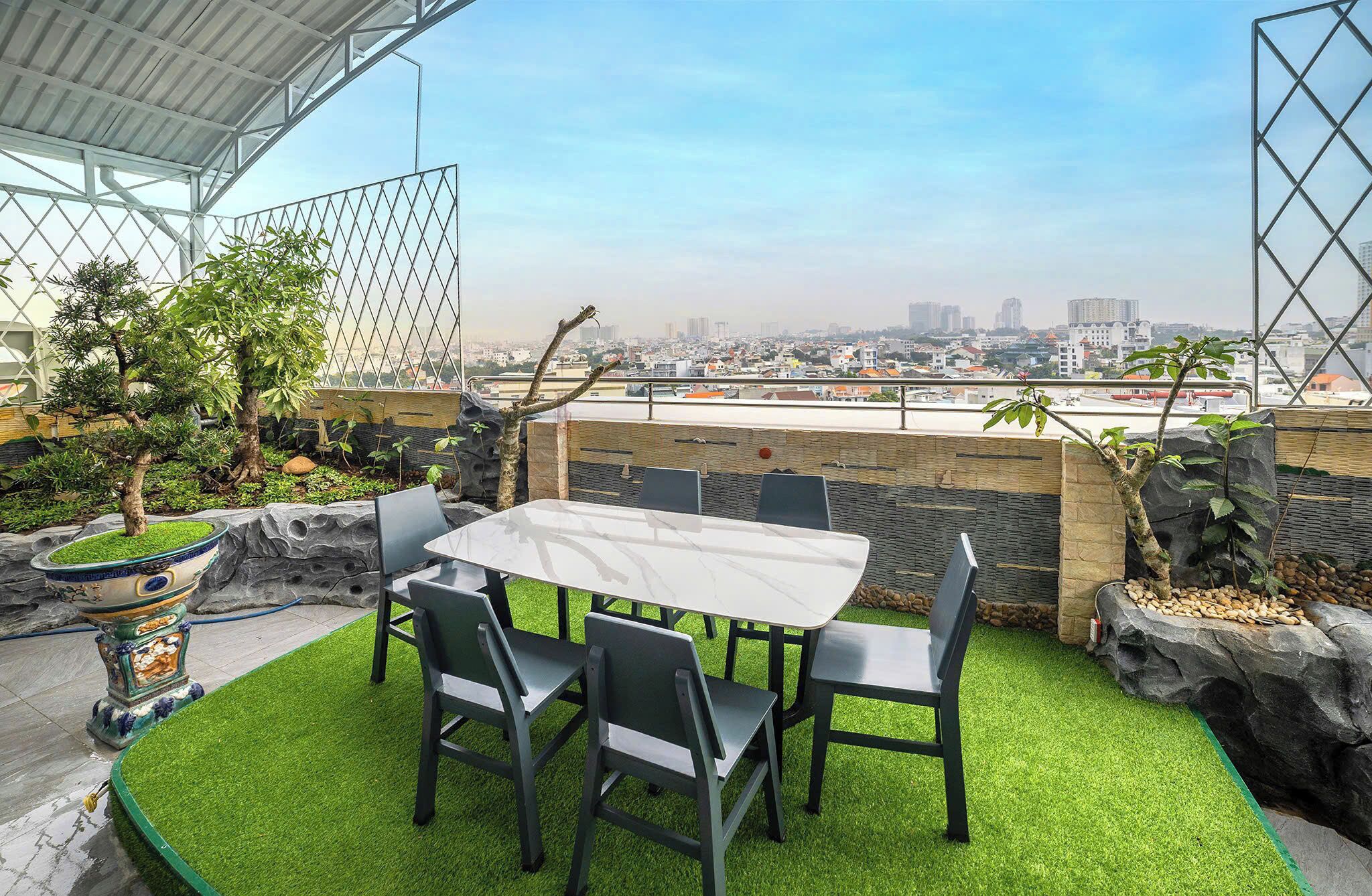 An outdoor patio with a table and chairs, surrounded by artificial grass, rocks, and plants.