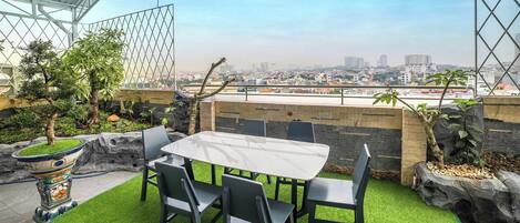 Une terrasse extérieure avec une table et des chaises, entourée de gazon synthétique, de rochers et de plantes.