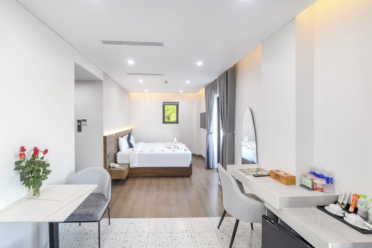 Una habitación de hotel moderna con cama, mesita de noche, silla, escritorio y una ventana pequeña.