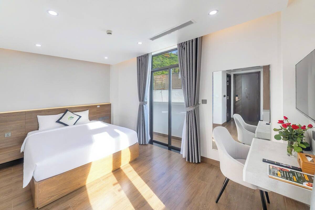 Habitación de hotel con cama, escritorio, silla, ventana con cortinas y puerta.