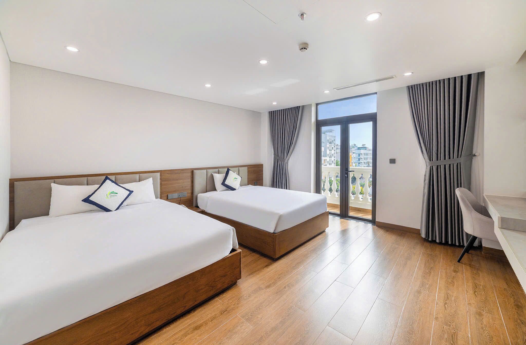 Een hotelkamer met twee bedden, een bureau en een balkon met gordijnen.