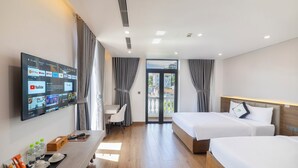A hotel room with two beds, a desk, a TV mounted on the wall, and a view of the outside through a glass door. - Green LP Hotel & Apartment (Ho Chi Minh City)