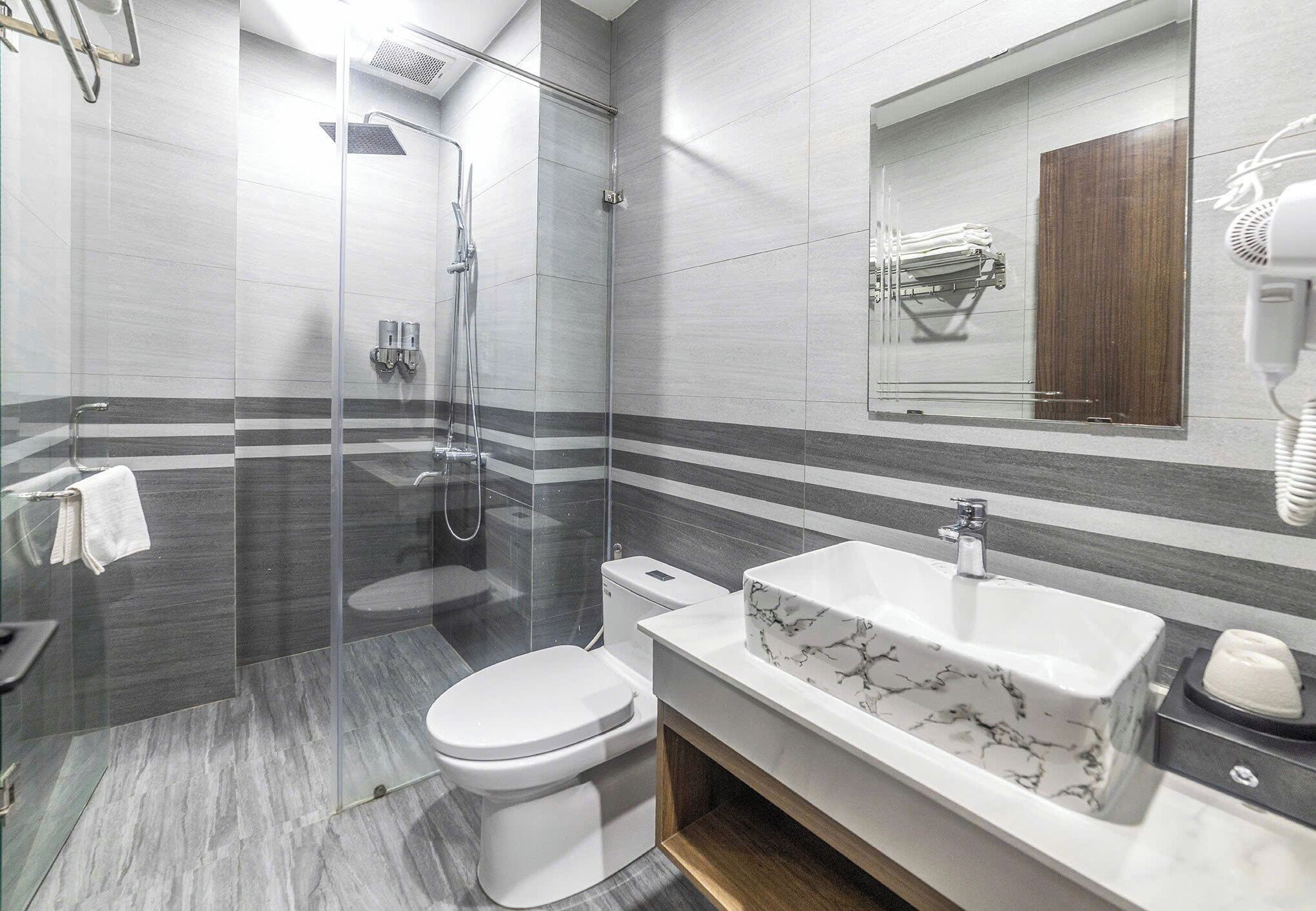 A modern bathroom with a glass-enclosed shower, a white toilet, a marble sink, and a towel rack.