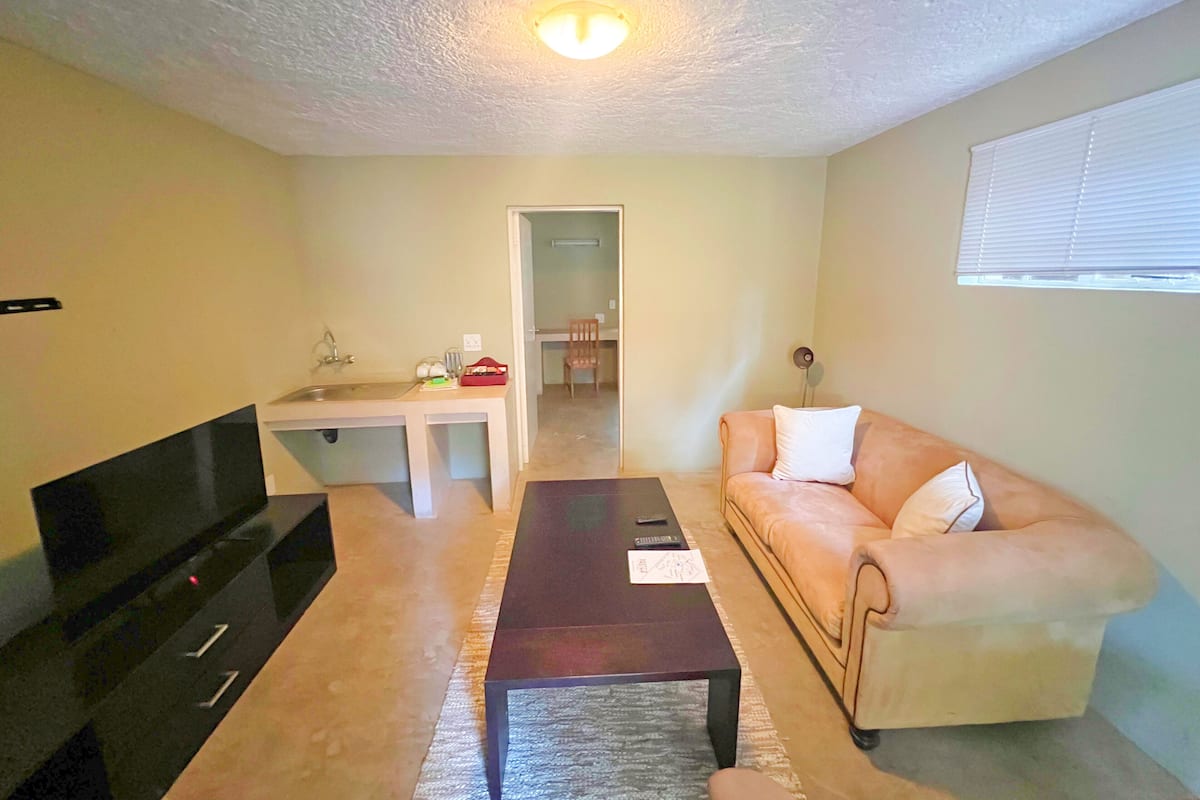 A living room with a TV, a sofa, a coffee table, and a kitchen area in the background.