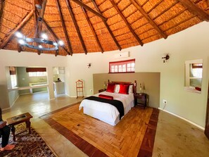 A spacious bedroom with a large bed, a wooden ceiling, and a view of the kitchen. - Protea Ridge Guest Cottages (Roodepoort)