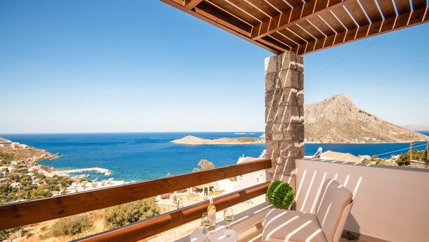 Un balcon avec vue sur la mer, un pilier en pierre et une table avec des verres et une bouteille.