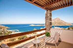 A balcony with a view of the sea, a stone pillar, and a table with glasses and a bottle.