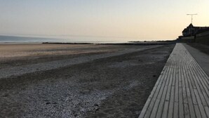 A beach with a wooden boardwalk and a building in the background. - Maison vue mer à Bénerville (bénerville sur mer)