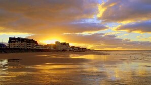 Une plage avec des bâtiments en arrière-plan, au coucher du soleil.