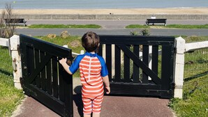 Un enfant se tient près d’une barrière, d’où l’on peut admirer la plage et l’océan.