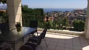 A balcony with a glass table and chairs, offering a view of a coastal town and the sea. - Anavyssos Dream Villa Sea View and Pool (Saronikos)