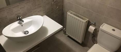 Une salle de bain avec un lavabo, des toilettes et un radiateur, le tout de couleur blanche.