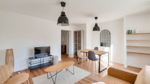 A modern living room with a TV, sofa, dining table, and chairs. There are two pendant lights, a bookshelf, and a large mirror. - Splendide T3 au Coeur de Marseille (Marseille)