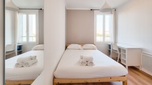 A minimalist hotel room with a single bed, a desk, and a chair. - Splendide T3 au Coeur de Marseille (Marseille)