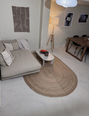 A modern living room with a sofa, a small coffee table with books and a cactus, a lamp, and a dining table with chairs. - Nomad Gardet Hostel (Stockholm)
