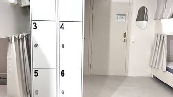 Une chambre d’hôtel dotée d’une grande armoire numérotée de 1 à 6, d’un lit avec une tête de lit, d’un tapis rond en fibres tressées et d’une porte avec une pancarte.