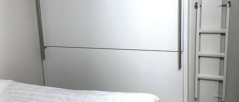 A bedroom with a bed, a wardrobe, and a built-in ladder.