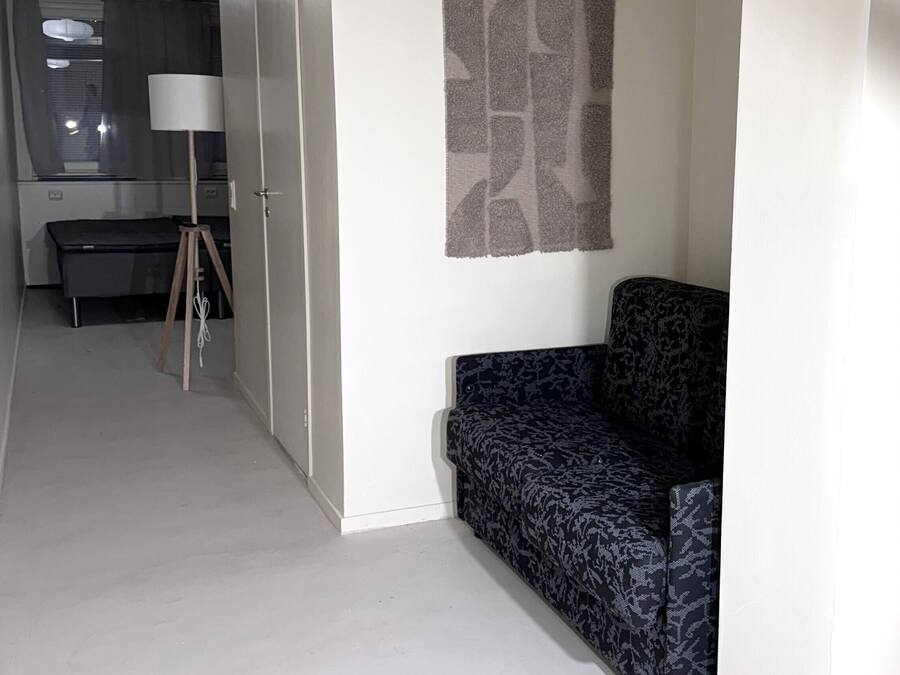 Una sala moderna con un sofá estampado, una lámpara y vistas a la cocina.